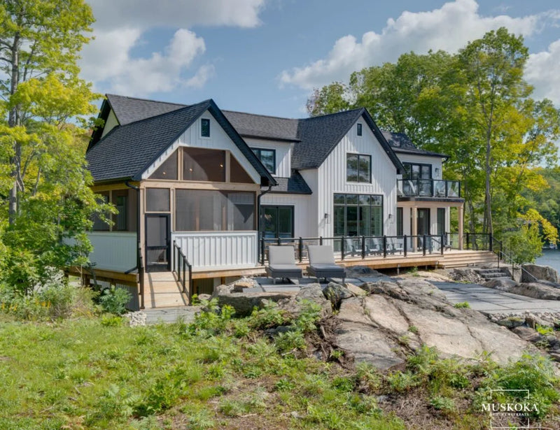 Modern house by a lake with trees and rocks in the foreground
