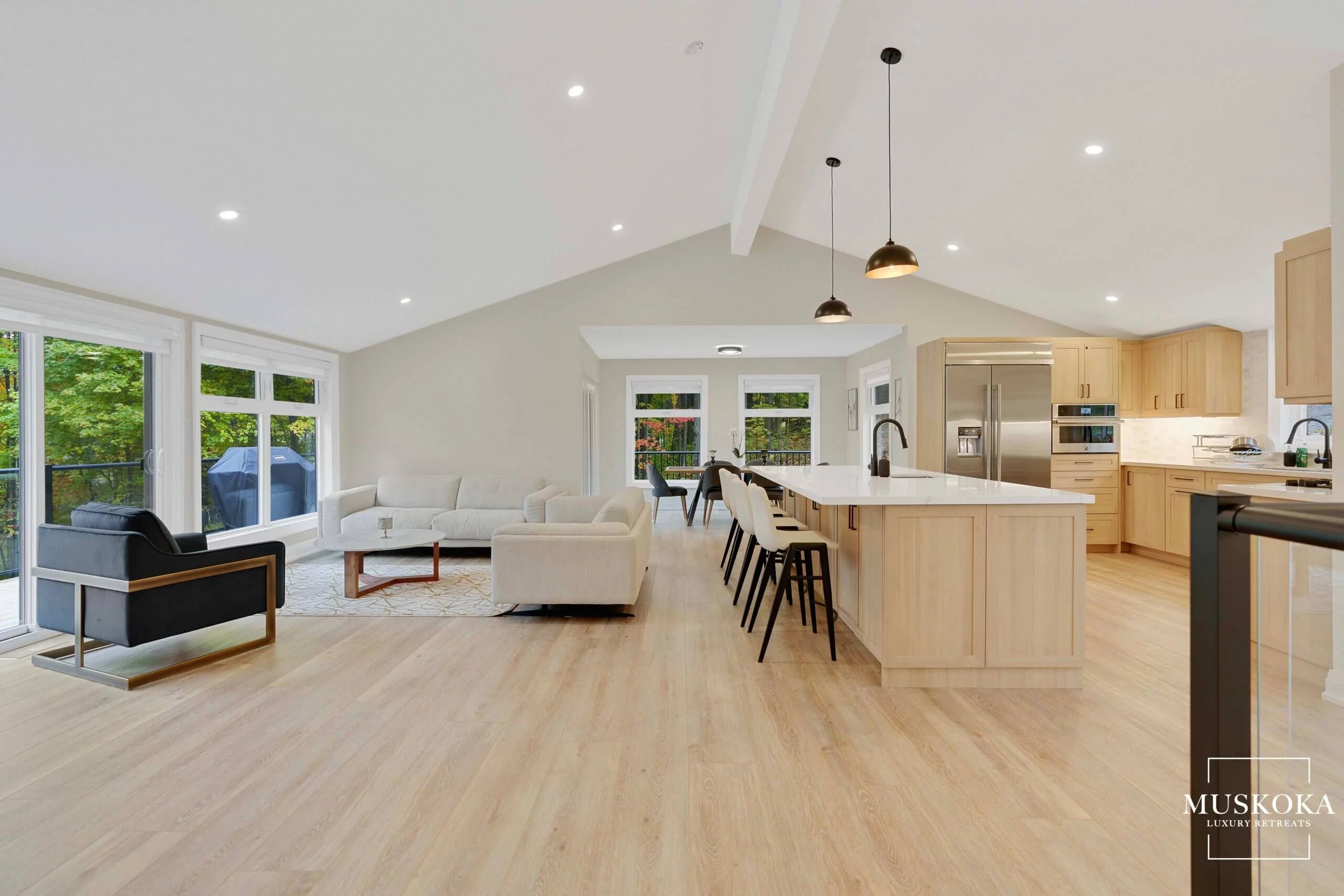 Modern open-plan kitchen and living room with wooden floors and large windows.