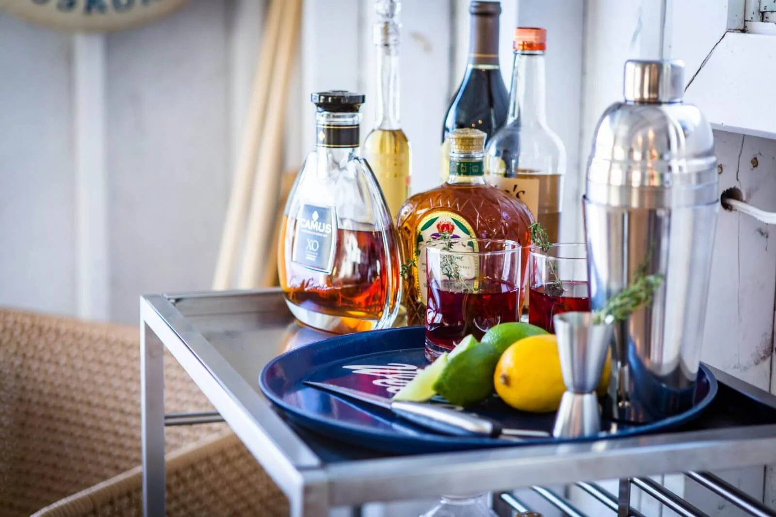 Bar cart with alcohol bottles, a cocktail shaker, and ingredients on a tray.