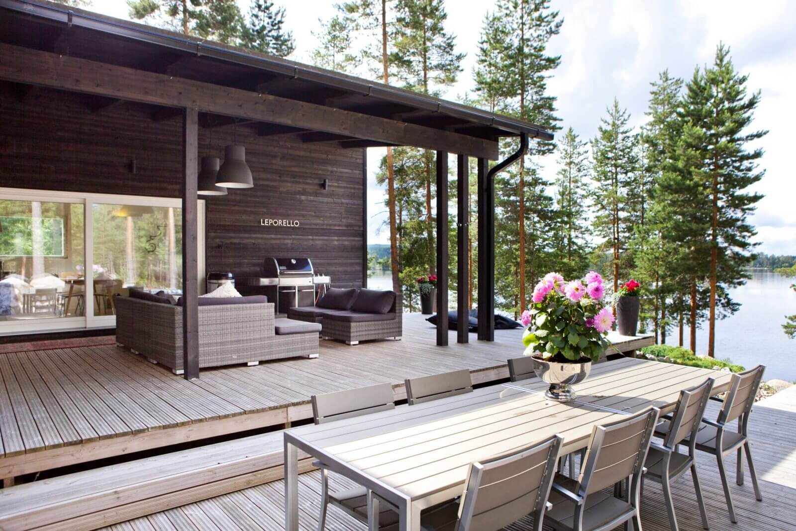 Outdoor deck with furniture and grill area near a body of water with trees in the background