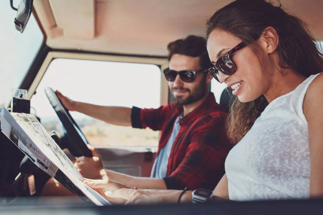 Man and woman in a car, looking at a laptop together.