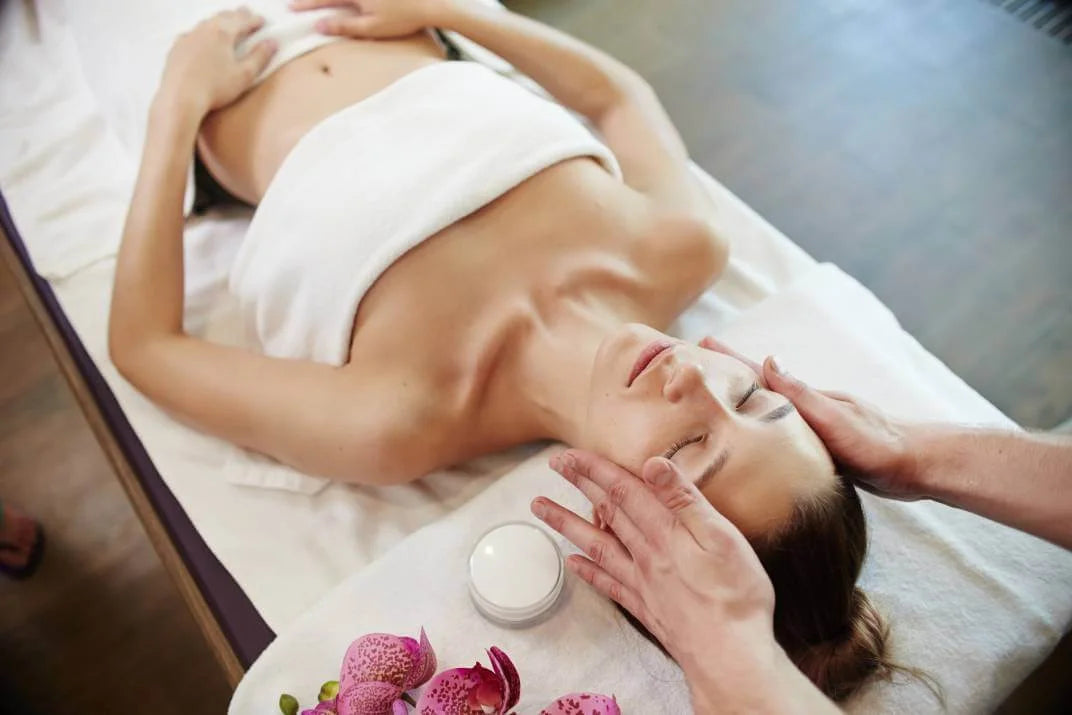 Woman receiving a facial massage in a spa setting with flowers and a candle.
