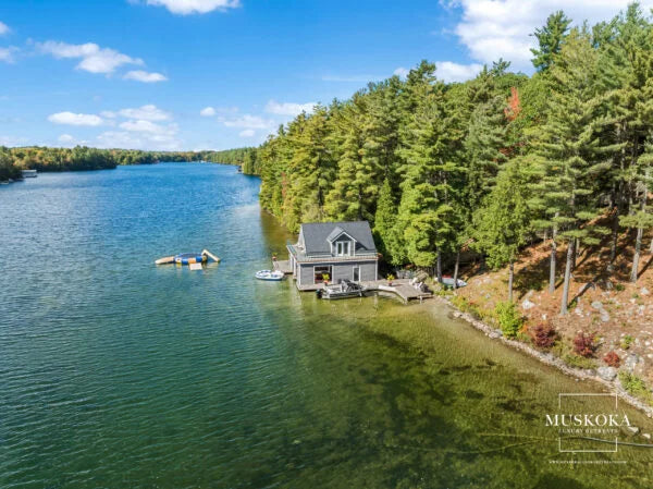 Cottage on a lake surrounded by trees with 'Muskoka' branding.