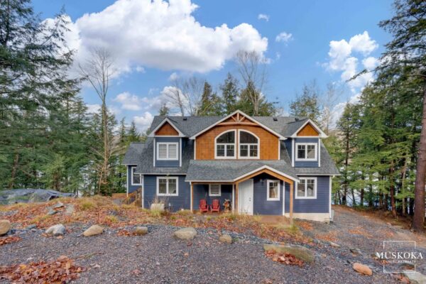Two-story house with blue and wood exterior in a forested area.
